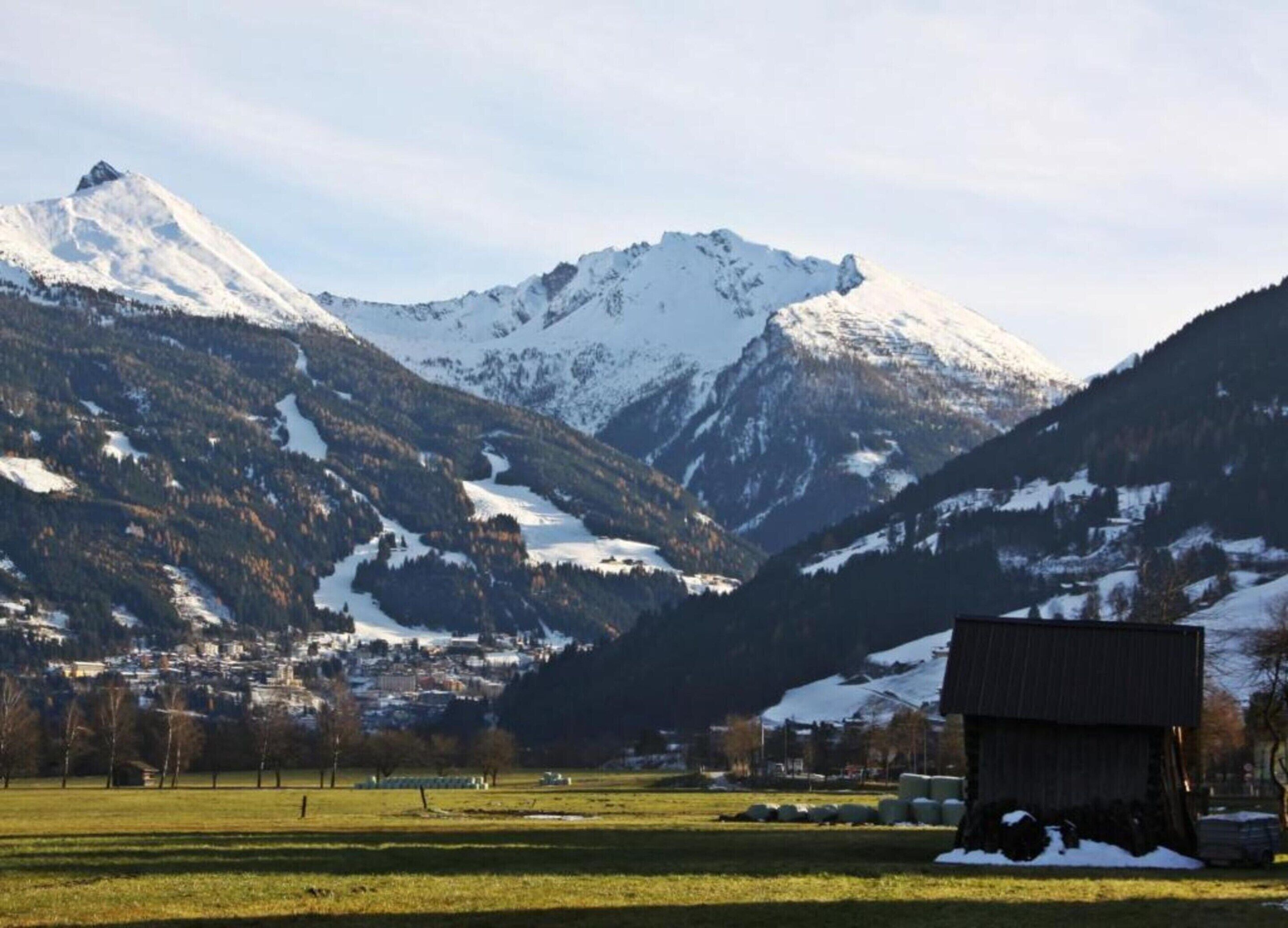 A rural landscape with a snow-covered mountain, a small building, and a field.