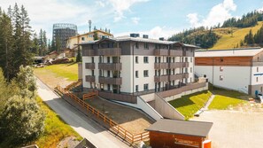 Un hotel de varios pisos con balcones, una zona de estacionamiento y vistas a un paisaje montañoso.