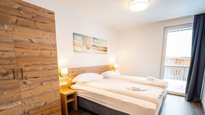 A bedroom with a wooden wardrobe, a bed with white linens, a painting on the wall, and a balcony with a view. - Comfortable Apartment in Katschberghohe (Rennweg am Katschberg)
