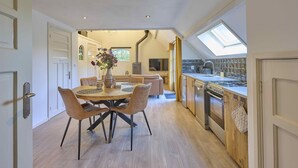 A modern kitchen with a skylight, wooden flooring, and a dining area with a table and chairs.