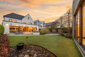 A modern house with a well-maintained lawn, a patio with outdoor seating, and a large glass door on the right side. - Whitstable | 4 bd | Pool | Games Room | Cinema (Kent)