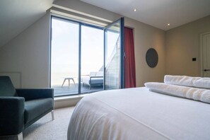 A hotel room with a large bed, a chair, a small table, and a view of the outside. - Whitstable | 4 bd | Pool | Games Room | Cinema (Kent)