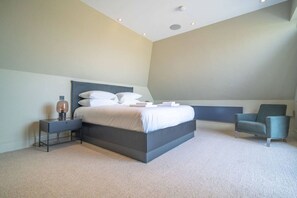 Quarto moderno com uma cama grande, mesa de cabeceira, cadeira e escrivaninha.