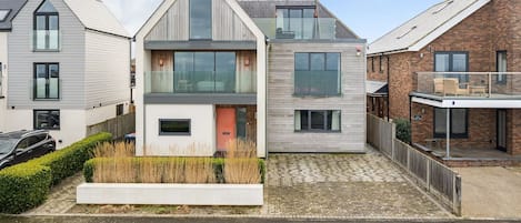 A modern two-story house with a flat roof, large windows, and a visible balcony.