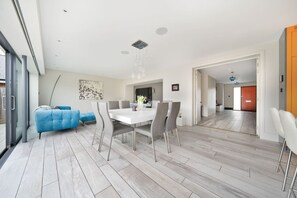 A modern dining area with a white table and grey chairs, a blue sofa, and a wooden floor. - Whitstable | 4 bd | Pool | Games Room | Cinema (Kent)