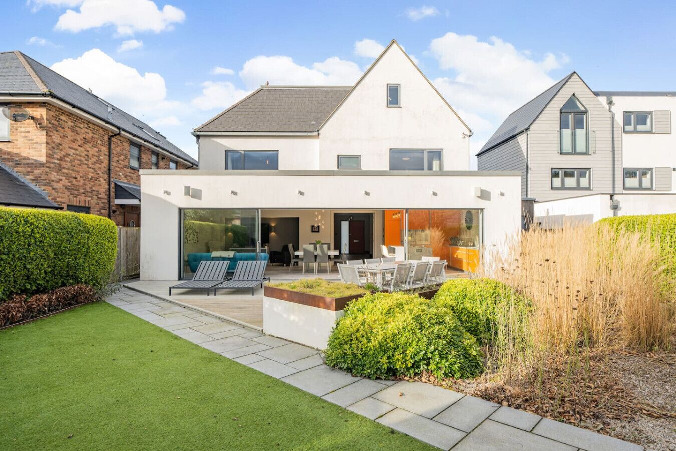 A modern two-story house with a patio area, a dining table, and outdoor seating.