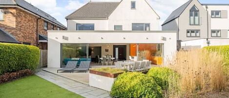 A modern two-story house with a patio area, a dining table, and outdoor seating.