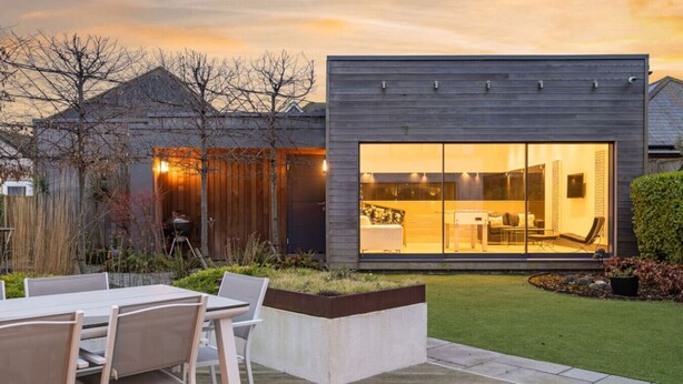 A modern house with a large glass window, a patio with chairs, and a well-maintained lawn. - Whitstable | 4 bd | Pool | Games Room | Cinema (Kent)
