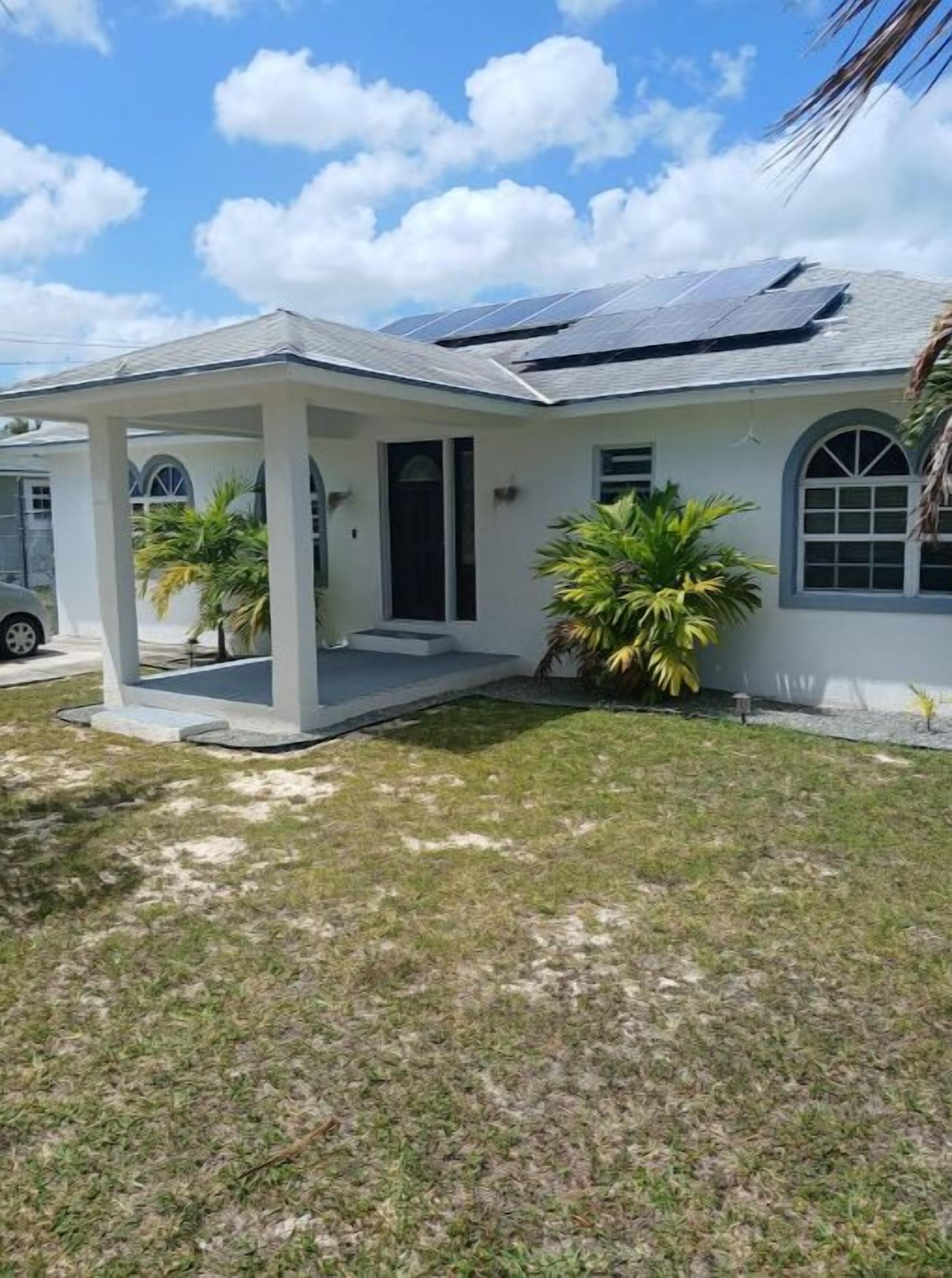 Uma casa térrea com varanda coberta, garagem e um pequeno jardim com palmeiras.
