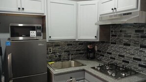 Een moderne keuken met witte kasten, een roestvrijstalen koelkast, een magnetron, een gasfornuis en een betegelde spatwand.