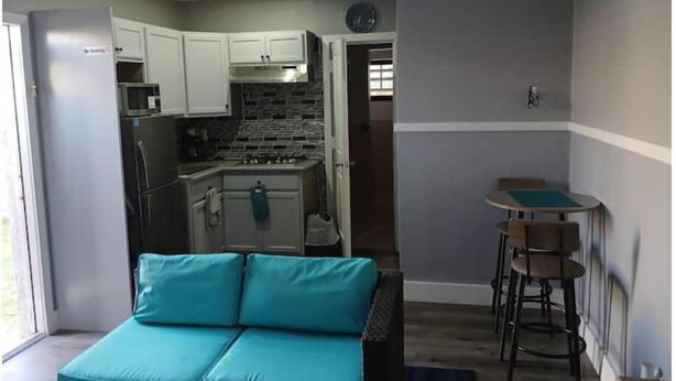 Un espacio habitable compacto con kitchenette, un sofá color turquesa y una pequeña zona de comedor.