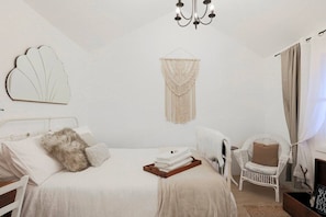 Ein Schlafzimmer mit einem Bett, einem Sessel, einer Wanddekoration aus Makramee und einer Chandelier.