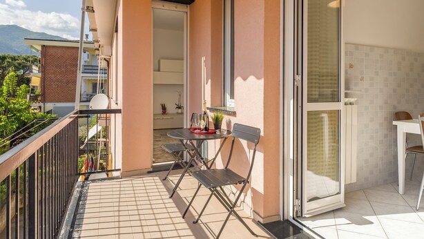 A balcony with a table and chairs, a sliding glass door, and a view of the mountains. - Quadri D'oro (Loano)