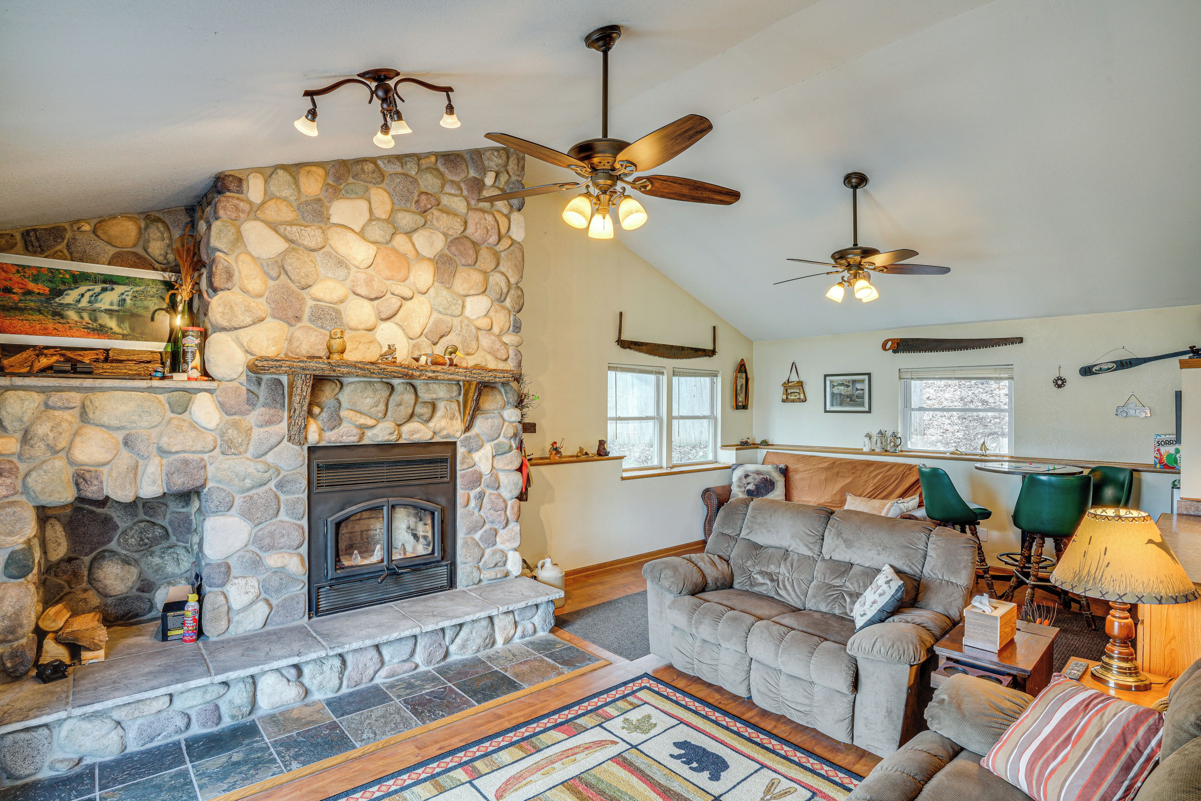 A cozy living room with a stone fireplace, a ceiling fan, and a comfortable seating area.