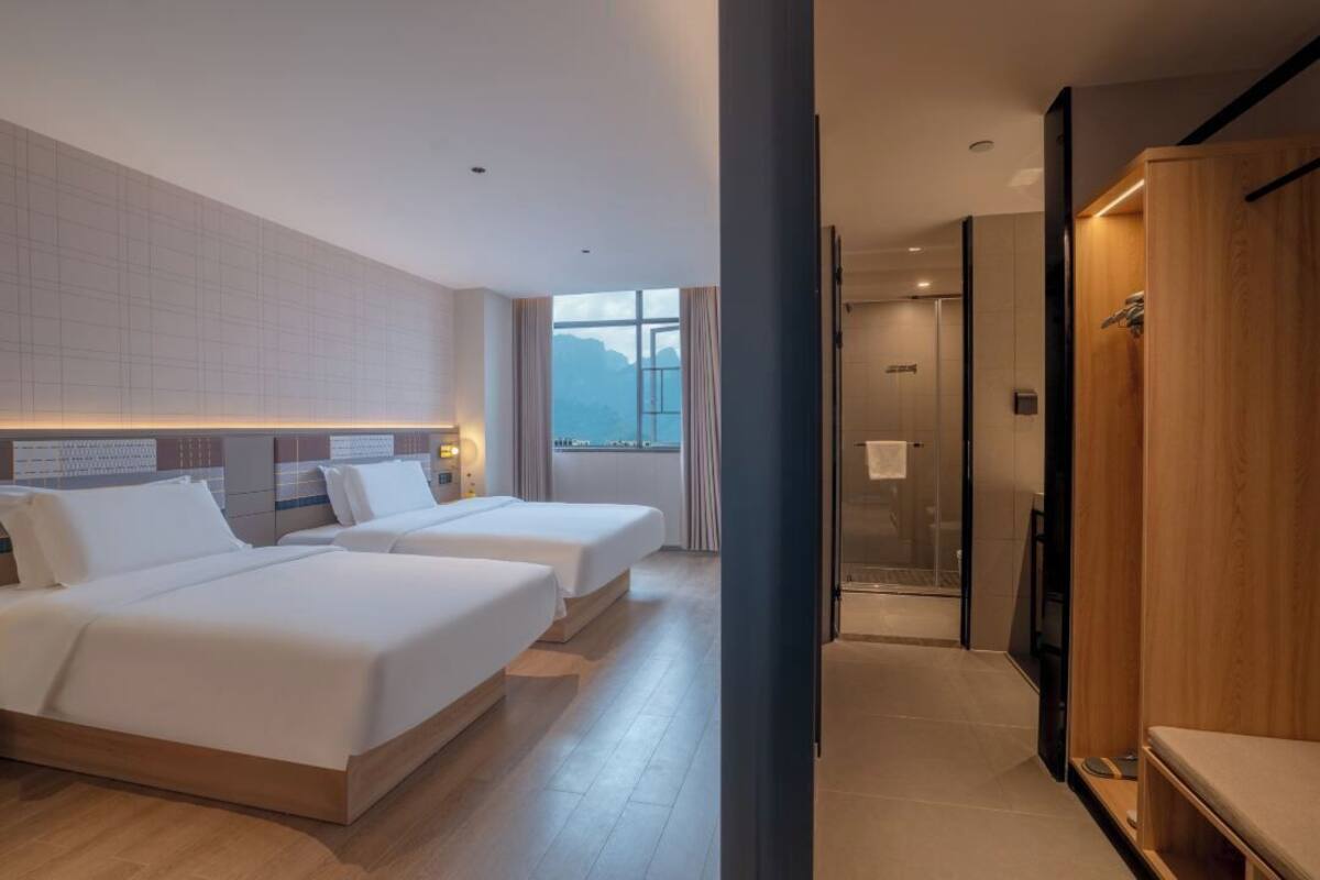 A hotel room with two beds, a large window, and a shower area.