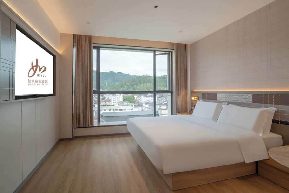 A hotel room with a large window, a bed, and a TV on the wall.