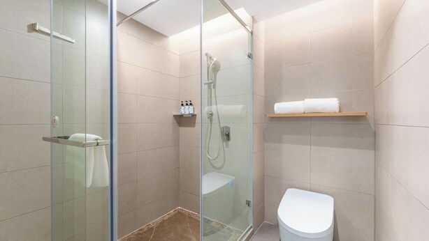 Un baño moderno con ducha de vidrio, inodoro y estante con artículos de aseo.