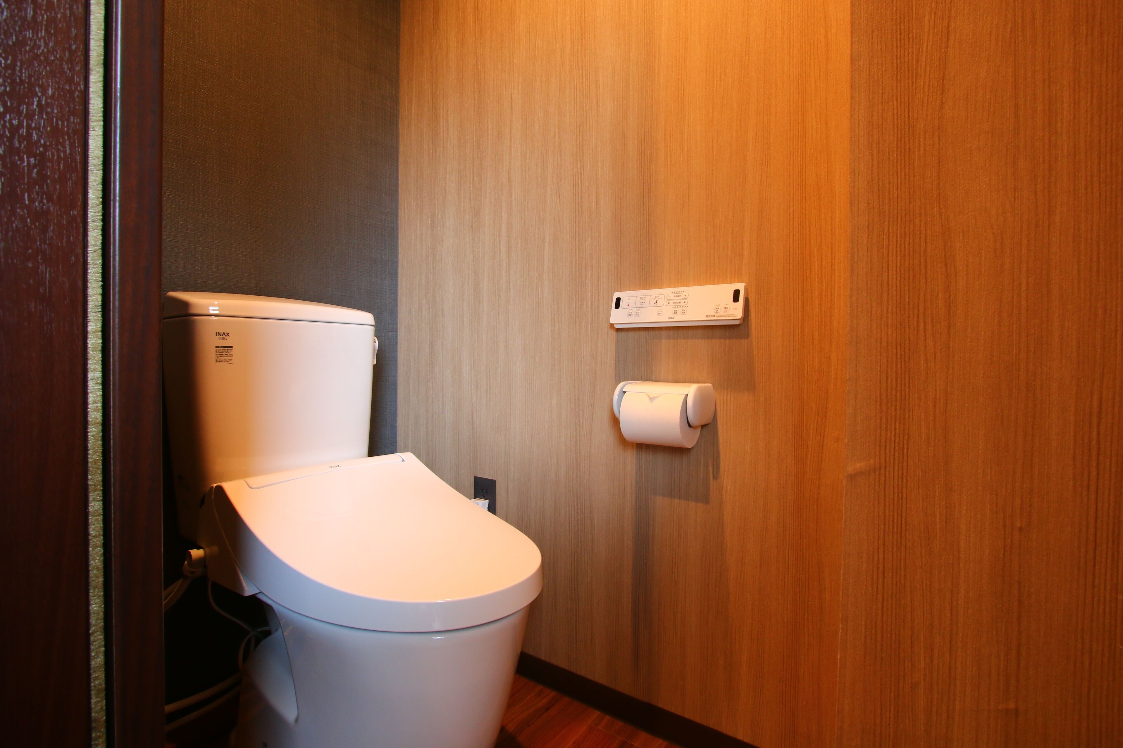 A modern bathroom with a white toilet, a paper towel dispenser, and a wooden wall.
