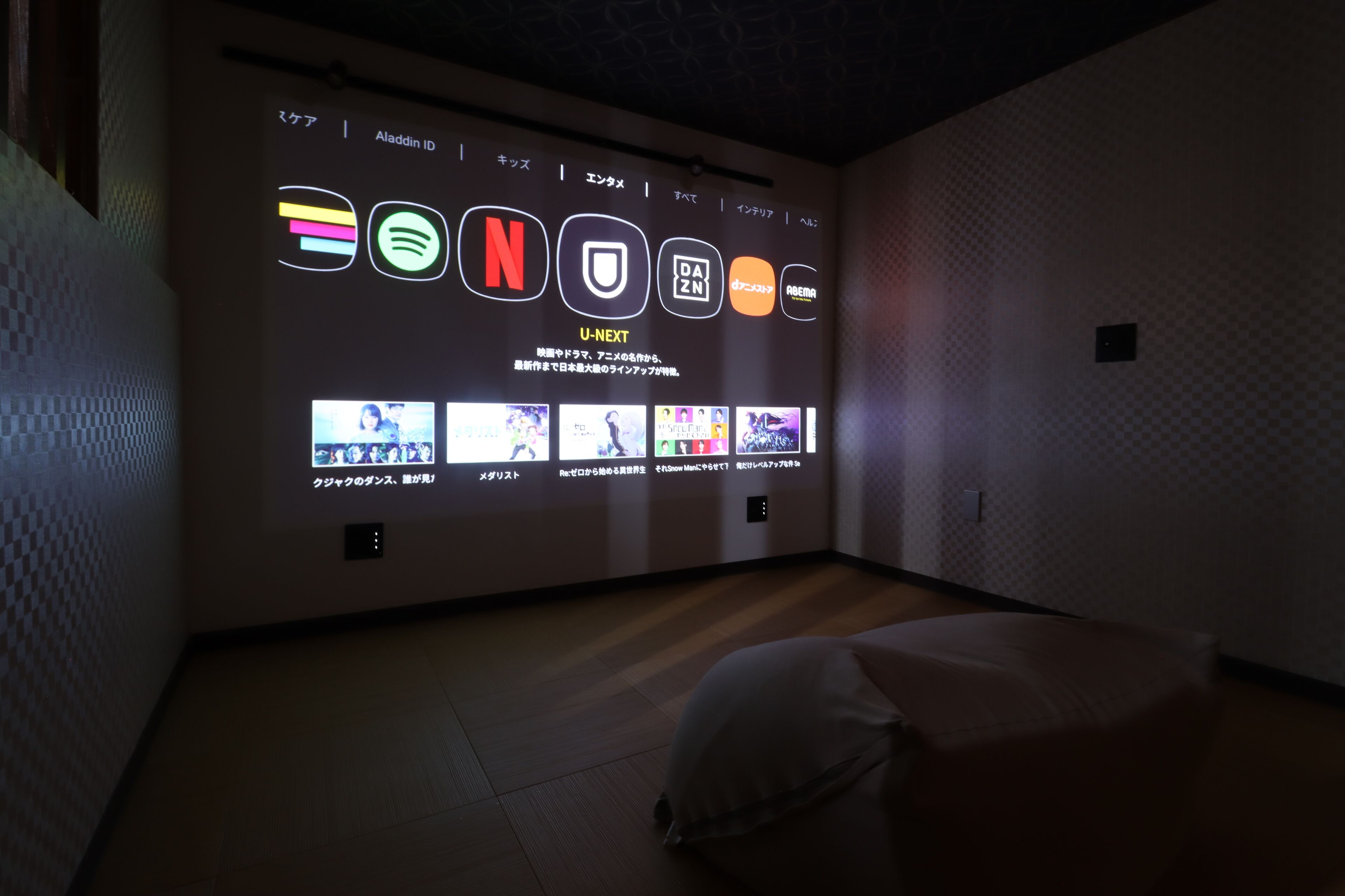 A room with a wall-mounted display featuring various media icons and a selection of video thumbnails.