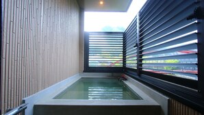 A modern bathroom with a rectangular bathtub, a skylight, and a view of a train track. - Myoukenkan (Kirishima)