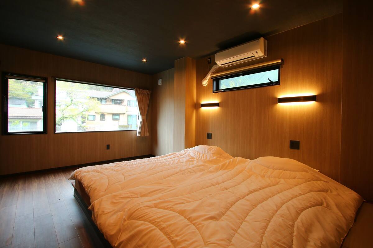 Une chambre avec un grand lit, des murs en bois et deux fenêtres.