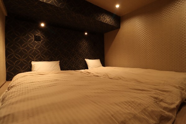 A bedroom with a patterned wall, a large bed with white bedding, and recessed lighting. - Myoukenkan (Kirishima)