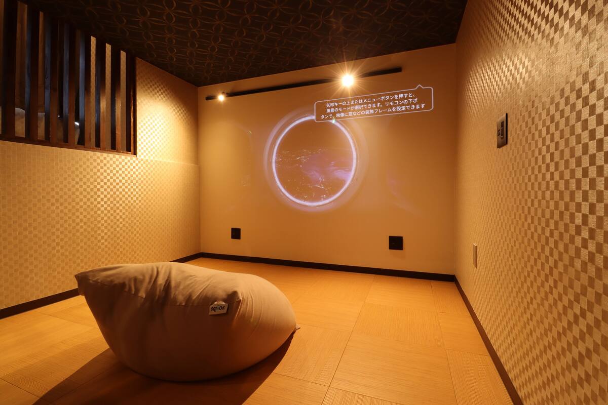 Une pièce dont un des murs est décoré d’un motif à carreaux, sur lequel est projetée une image circulaire, et qui contient un fauteuil en forme de sac de haricots.