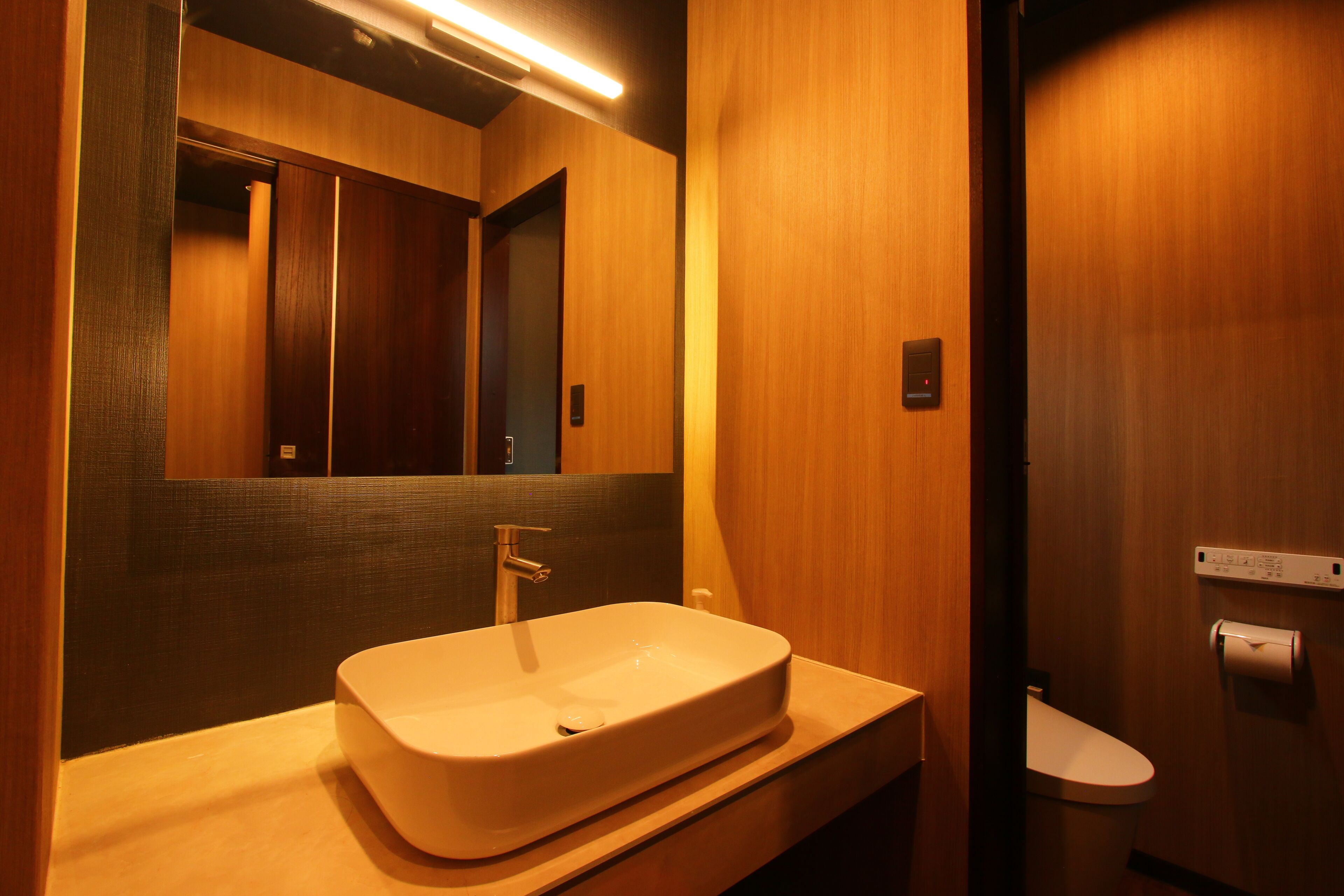 A modern bathroom with a wooden vanity, a large mirror, and a toilet.