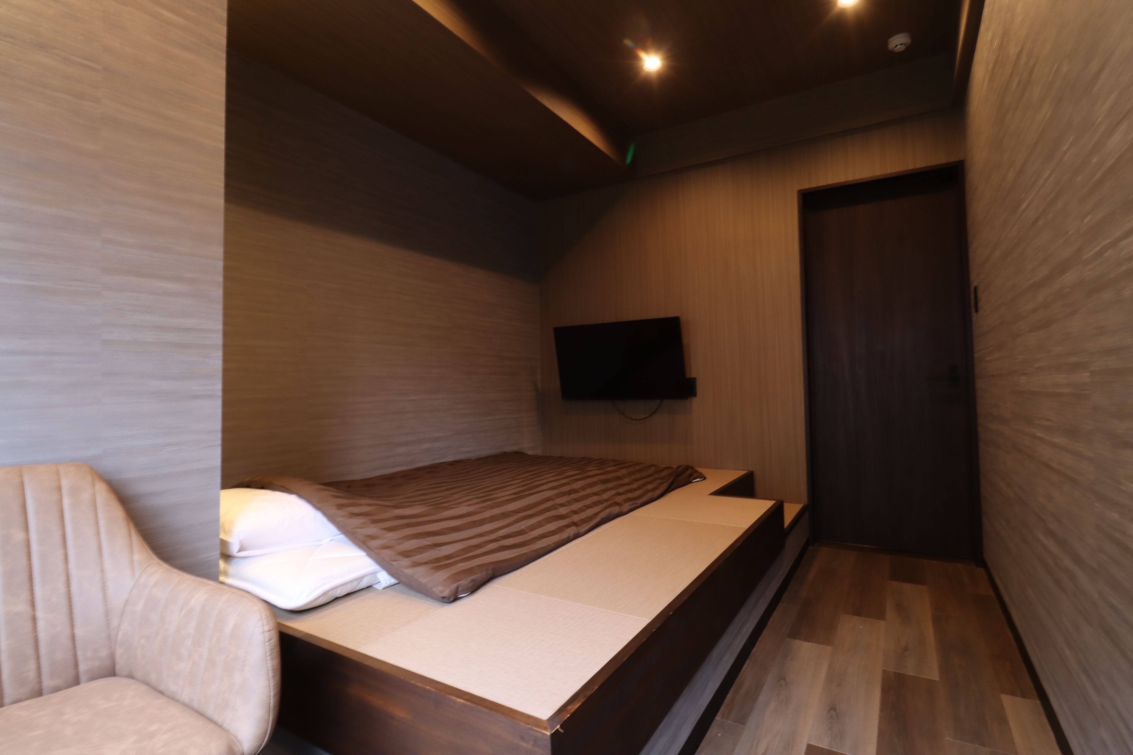 A modern bedroom with a bed, a chair, a flat-screen TV, and a wooden door.