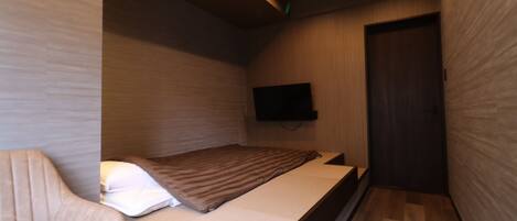 A modern bedroom with a bed, a chair, a flat-screen TV, and a wooden door.