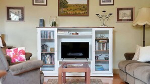 Uma sala de estar com televis ão, estantes de livros, mesa de centro e sofá.