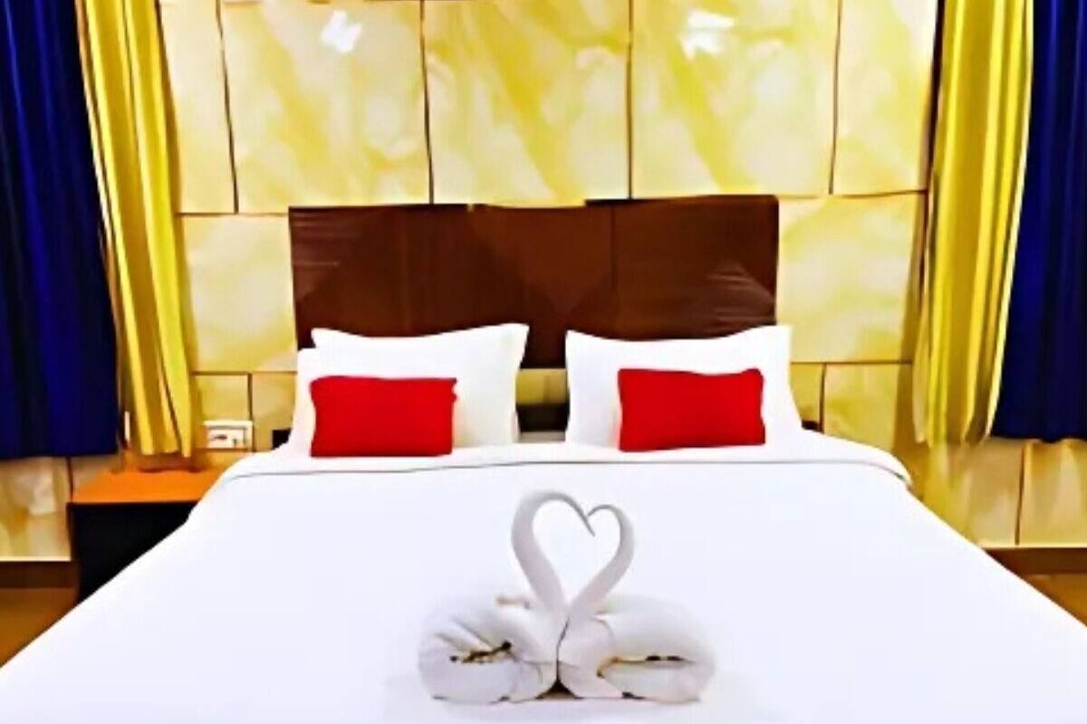 Habitación de hotel con una cama grande, ropa de cama blanca, almohadas rojas y una presentación de toallas con forma de corazón.
