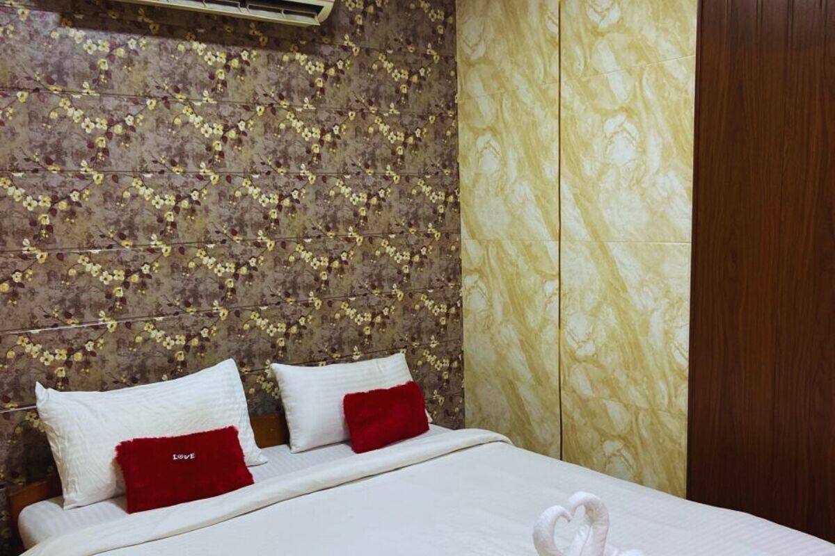 Una habitación de hotel con un cabecero estampado con motivos florales, una cama con ropa de cama blanca y almohadas rojas, y un cisne decorativo sobre la cama.