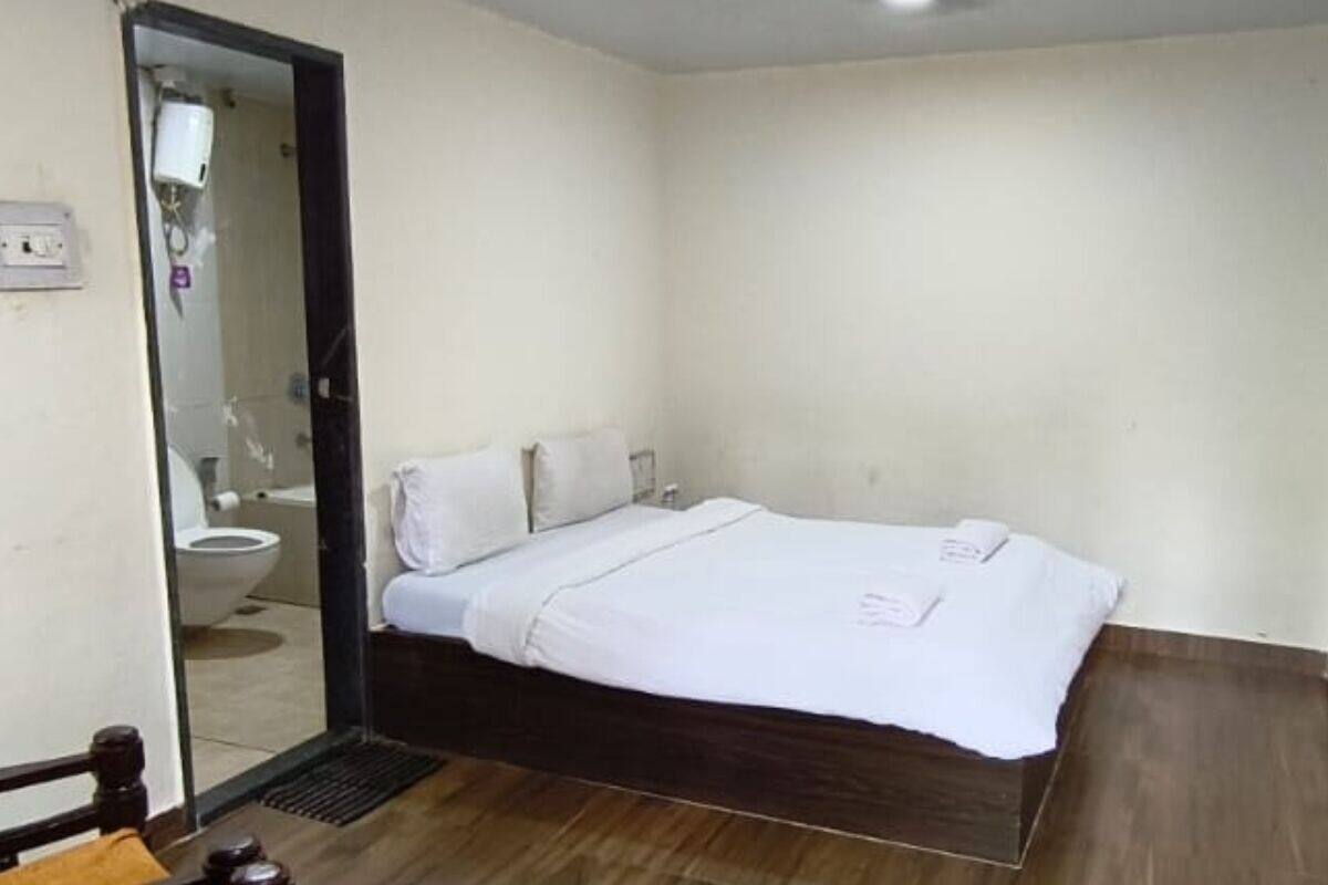 Un dormitorio con cama, piso de madera, pared blanca y puerta que da a un baño.