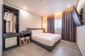 Et moderne hotelværelse med en seng, et skrivebord med computer, et fjernsyn og et garderobeskab.