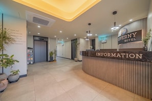 A hotel reception area with a reception desk labeled 'GIVENY HOTEL INFORMATION,' a directory on the wall, and potted plants. - Giverny Hotel (Gyeongju)