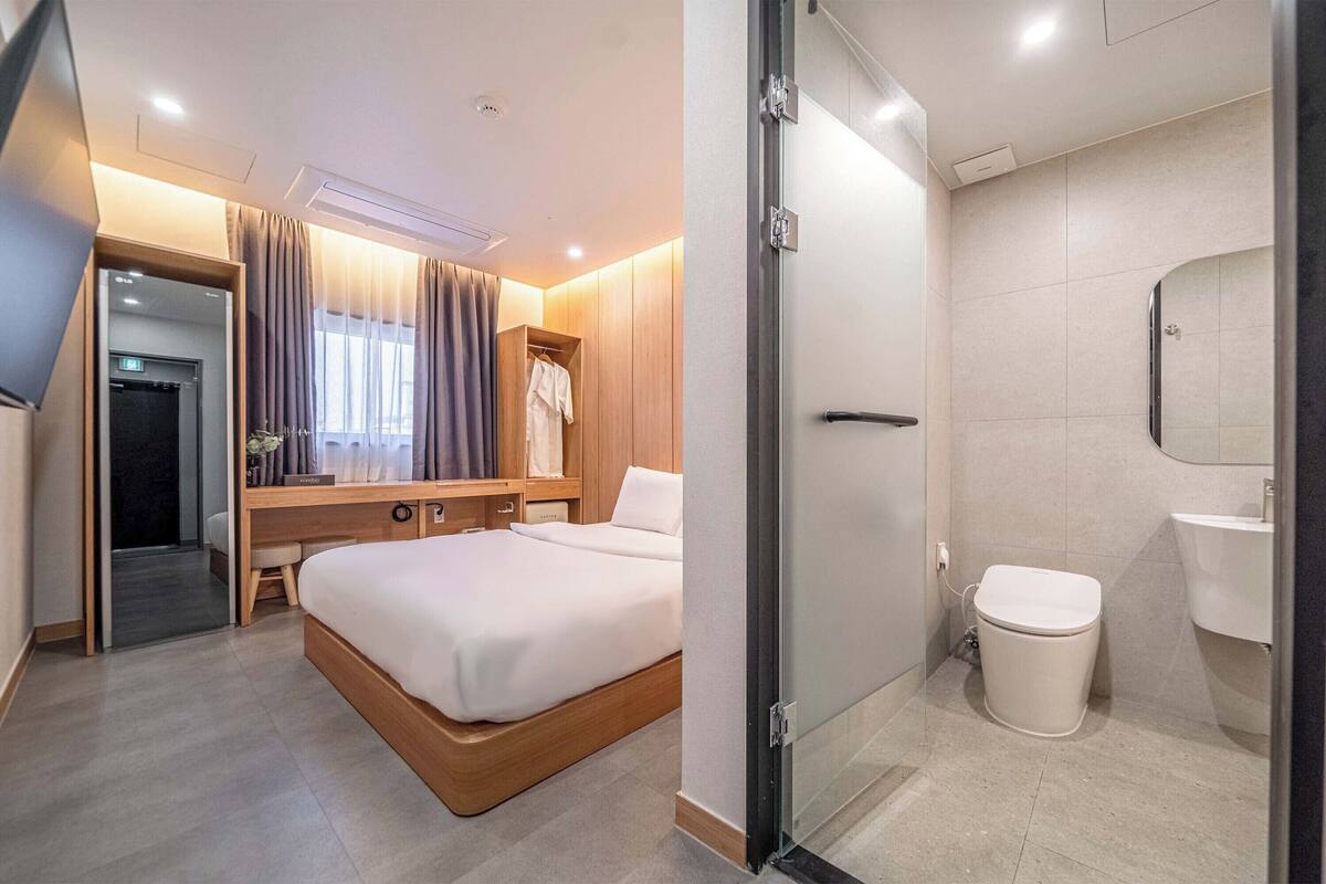 Una habitación de hotel moderna con una cama, una mesita de noche y zona de ducha.