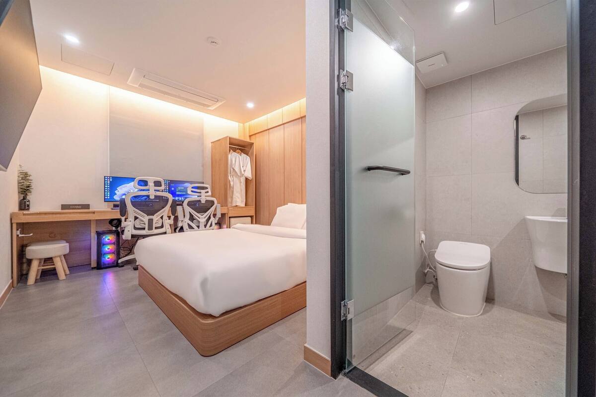 Una habitación de hotel moderna con cama, escritorio, ordenador, equipo de ejercicio y baño independiente.