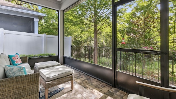 A balcony with wicker furniture, a white fence, and a view of trees and a garden. - Seashell Cove | Pet-friendly, Bikes, & Short walk to Egan's Creek! (Fernandina Beach)