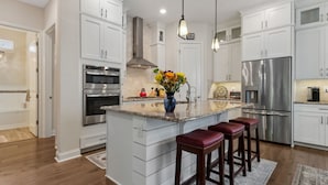 A modern kitchen with white cabinetry, stainless steel appliances, a central island with stools, and pendant lighting. - Seashell Cove | Pet-friendly, Bikes, & Short walk to Egan's Creek! (Fernandina Beach)