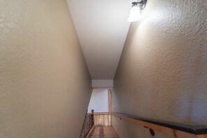A narrow stairway with a wooden handrail and a light fixture above.