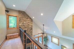 A high-ceilinged staircase with a stone wall and wooden railing, leading to an upper floor.