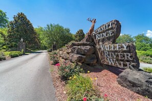 A sign for 'SUMMIT RIDGE VALLEY RIVER WALK' with a deer sculpture, surrounded by greenery and a paved path.