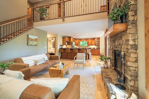 A spacious living area with a fireplace, a kitchen in the background, and a staircase leading to an upper level.