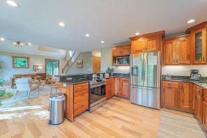 A modern kitchen with wooden cabinets, stainless steel appliances, and a central island. - Beautiful Cabin on 5 Acres • Pond • Decks • Close to Everything (Marble)