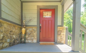 A red door with a window, a stone wall, and a wooden porch with a doormat.