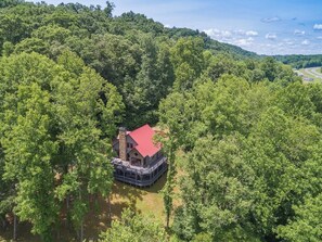 A cabin surrounded by dense forest, with a red roof and a stone chimney.