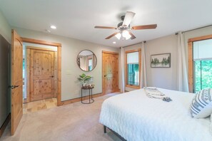 A bedroom with a bed, a ceiling fan, wooden doors, a window, and a wall-mounted mirror. - Beautiful Cabin on 5 Acres • Pond • Decks • Close to Everything (Marble)