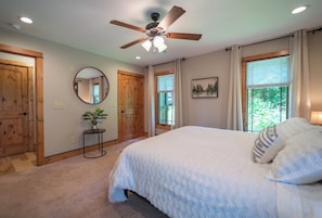 Quarto com cama, ventilador de teto, janelas e porta.