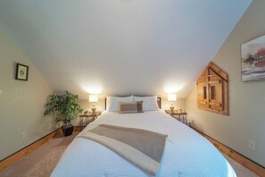 A bedroom with a large bed, a potted plant, bedside lamps, and a wooden headboard.